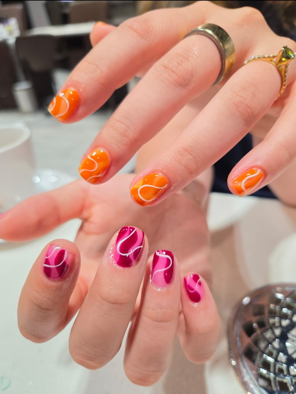 Short square nails in orange and magenta with white freehand swirls